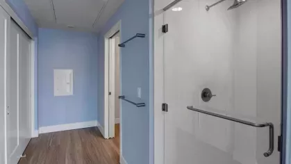 Modern bathroom with glass-enclosed shower and light blue walls at The Pacific Luxury Apartments.