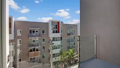 Modern glass balcony overlooking neighboring apartment buildings and lush palm trees.