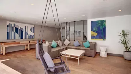 Modern lounge area at The Pacific Luxury Apartments featuring a cozy sectional sofa, swing chair, and vibrant contemporary art.