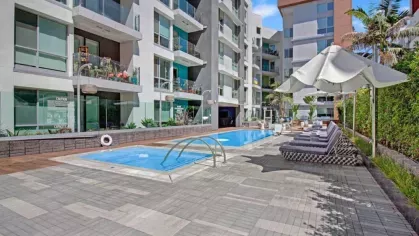 Sparkling pool surrounded by sun loungers and lush greenery at The Pacific Luxury Apartments' outdoor courtyard.