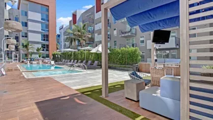 Covered cabana with lounge seating and TV, overlooking the pool area at The Pacific Luxury Apartments.