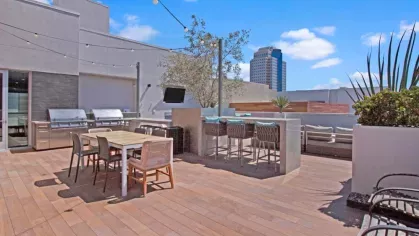 "Rooftop terrace at The Pacific Luxury Apartments featuring an outdoor dining area, built-in grills, bar seating, and string lighting against a backdrop of city views."