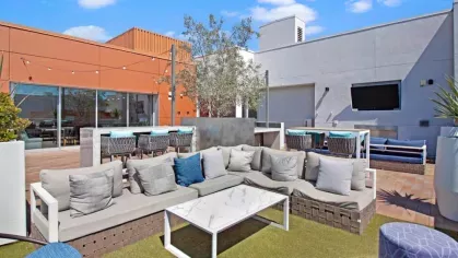 "Modern rooftop lounge at The Pacific Luxury Apartments with plush outdoor seating, green turf, bar seating, and a mounted television for entertainment."