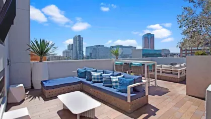 "Stylish rooftop seating area at The Pacific Luxury Apartments with cozy blue and white cushioned sofas, a high-top dining table, and panoramic cityscape views."