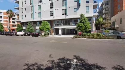 "Side entrance of The Pacific Luxury Apartments, highlighting modern design, available parking, and lush greenery for a welcoming arrival experience."