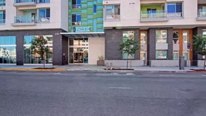 "Main entrance to The Pacific Luxury Apartments, featuring a vibrant green and blue facade, glass windows, and welcoming landscaping along the street."