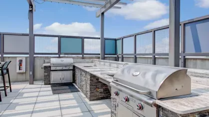 An outdoor grilling area with modern stainless steel grills and a pergola overhead.