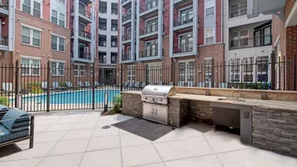 A courtyard featuring a swimming pool, lounge chairs, and a built-in outdoor kitchen with grills.