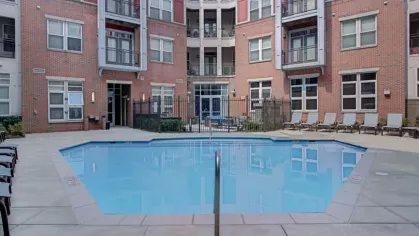 A gated pool area in a courtyard surrounded by apartment balconies and red brick walls.