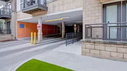 A driveway entrance to a parking garage with a yellow clearance bar and adjacent balconies.