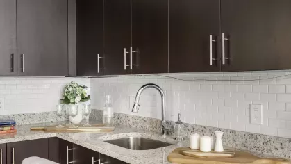 A modern kitchen with dark cabinets, stainless steel appliances, a center island, and an adjacent open living space filled with natural light.