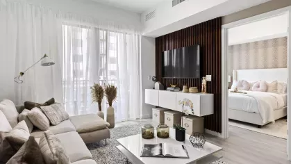 A cozy living room with plush beige seating, soft throw pillows, and a large window with sheer curtains allowing sunlight to brighten the space.