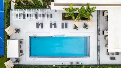 Aerial view of the Pine Ridge Luxury Apartments showing a vibrant blue basketball court, a sparkling rectangular swimming pool, and surrounding landscaped greenery.