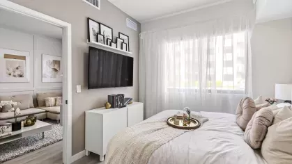 A modern bedroom featuring a mounted flat-screen TV, a sleek white console, and elegant decor at Pine Ridge Luxury Apartments.