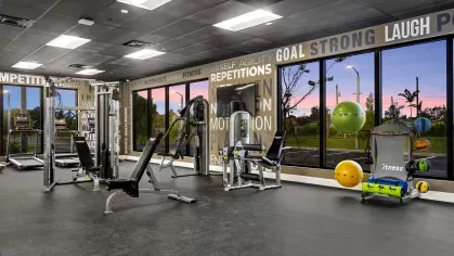 A twilight view of the fitness center with a variety of workout equipment, showcasing a motivational and well-lit space for residents.
