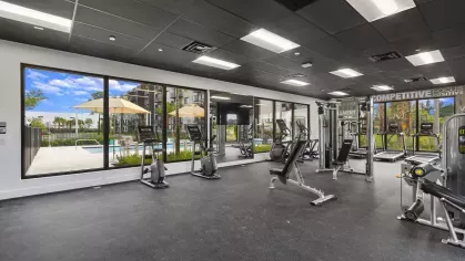 A fully equipped fitness center at Pine Ridge Luxury Apartments featuring cardio machines, strength equipment, and large windows overlooking the pool area.