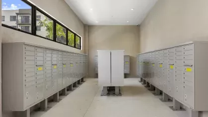 A secure mailroom with neatly arranged individual mailboxes and windows that provide natural light.