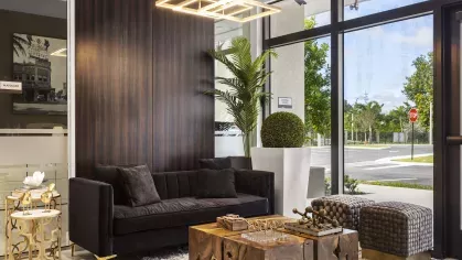 A modern lounge area featuring a sleek black sofa, a unique wooden coffee table, and floor-to-ceiling windows that let in natural light at Pine Ridge Luxury Apartments.