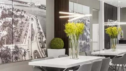 A stylish dining space with white tables, gray chairs, and decorative green plants against a backdrop of vintage black-and-white wall art.