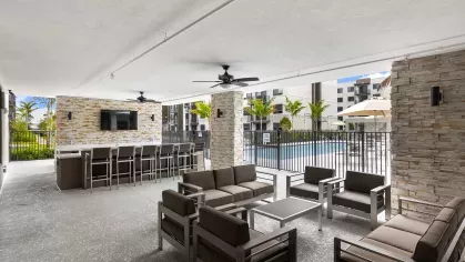 A spacious covered patio with modern furniture, ceiling fans, and a direct view of the sparkling swimming pool and landscaped surroundings.