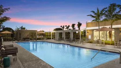 A resort-style pool at sunset with poolside seating, cabanas, and lush palm trees, creating a tranquil retreat for residents.