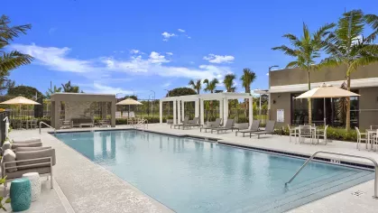 A crystal-clear pool surrounded by lounge chairs, umbrellas, and cabanas, ideal for relaxation under the sunny blue sky.