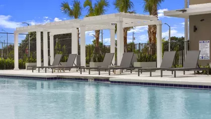 A pristine swimming pool in front of a modern clubhouse with lounge chairs arranged around the pool deck, showcasing luxurious amenities at Pine Ridge Luxury Apartments.