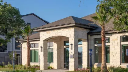 Grand clubhouse exterior with stone-accented architecture, lush landscaping, and a welcoming entrance that sets the tone for luxury living.