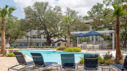 Resort-style pool with lounge chairs, blue umbrellas, and lush landscaping, creating a tranquil outdoor retreat for residents.