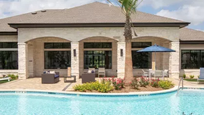 Clubhouse exterior at Vista At Town Green, featuring elegant stone architecture, large windows, and a beautifully landscaped pool area for residents to enjoy.