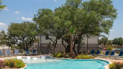 Expansive swimming pool with crystal-clear water, surrounded by lush greenery, lounge chairs, and towering oak trees, creating a peaceful outdoor oasis.