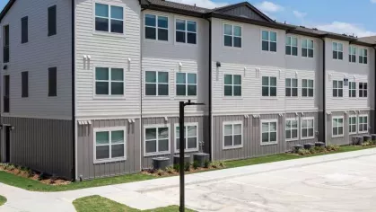 A modern three-story apartment building with stylish gray siding, large windows, and a well-maintained landscape, showcasing the contemporary living spaces at Vista At Town Green.