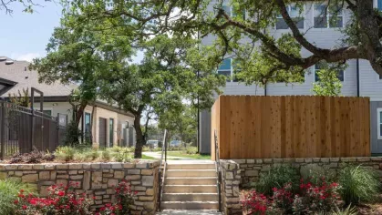 Beautifully landscaped walkway lined with stone walls, colorful flowers, and mature trees, leading to community amenities at Vista At Town Green.