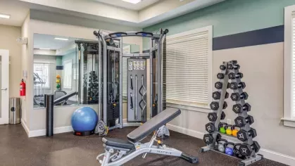 A well-equipped gym at Oak Enclave Luxury Apartments with a weight station, free weights, and an adjustable workout bench, offering residents a private fitness experience.