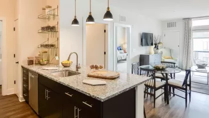 Modern kitchen with granite countertops, dark cabinetry, and pendant lighting, seamlessly connecting to the dining and living areas.