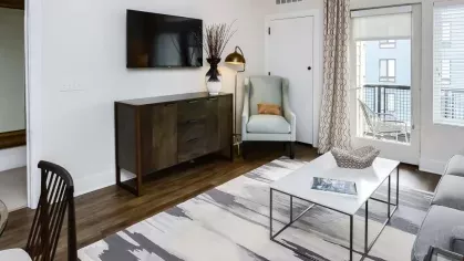 Light-filled living room with cozy seating, a flat-screen TV, and direct access to the outdoor balcony with a modern aesthetic.