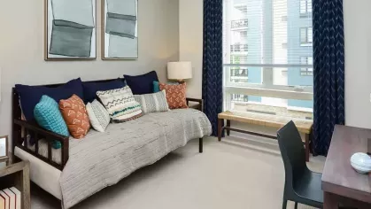 Bright and welcoming home office or guest room with a daybed, workspace, and large window at Riverworks Luxury Apartments.