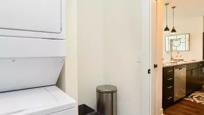 Compact laundry area with a stacked washer and dryer, adjacent to a modern kitchen at Riverworks Luxury Apartments.