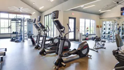 "Spacious gym at Riverworks Luxury Apartments with cardio machines, strength equipment, and expansive windows for natural lighting."