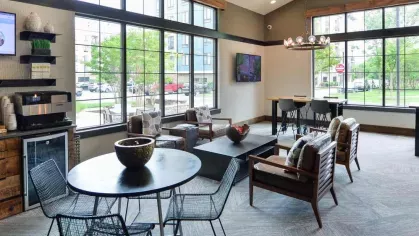 "Community lounge at Riverworks Luxury Apartments with contemporary furniture, a large TV, and ample natural light from floor-to-ceiling windows."