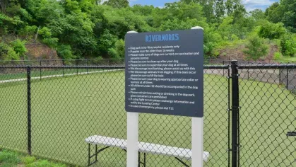 Gated dog park with green turf and signage, offering a dedicated space for pet-friendly activities at Riverworks Luxury Apartments.