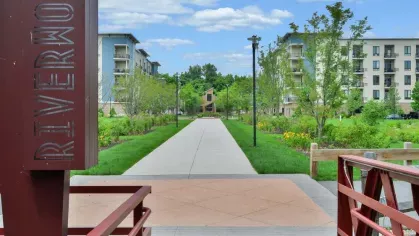 Riverworks entrance sign with a view of the community’s scenic walkway, connecting to the luxury apartment buildings through a charming red bridge and beautifully landscaped grounds.