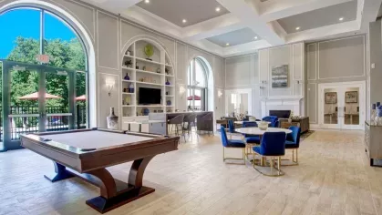 A stylish clubroom with high ceilings, a pool table, and comfortable seating, featuring large windows and access to outdoor spaces.