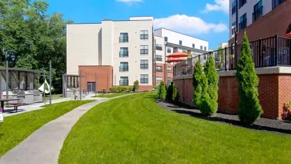 A vibrant green outdoor space with pathways, manicured shrubs, and community grilling areas at The Royal Belmont.