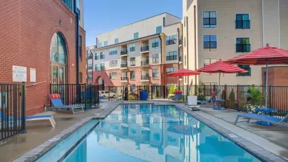 A closer view of the resort-style pool at The Royal Belmont, with red umbrellas, comfortable seating, and arched building entrances.