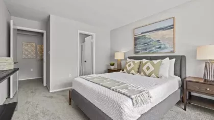 A contemporary bedroom with a gray upholstered bed, white linens, neutral décor, and an abstract beach painting above the headboard.