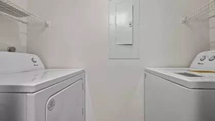 A compact laundry room with a white washer and dryer, wire shelving for storage, and a neutral color palette.
