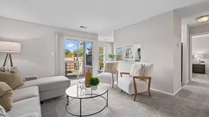 An open-concept living space with a sectional sofa, plush armchairs, a round glass coffee table, and a sliding door allowing in natural light.