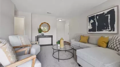 A contemporary living room with a gray sectional, textured throw pillows, wooden armchairs, and a decorative round mirror above a console table.