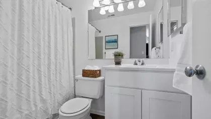 A clean and bright bathroom with a white vanity, a large mirror, modern lighting, and a bathtub with a white textured shower curtain.